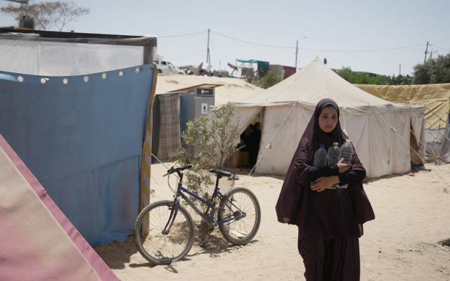 Duaa Abu Sabha holds water bottles while walking to her tent in the Al-Mawasi area in Khan Yunis Governorate. Duaa Abu Sabha holds water bottles while walking to her tent in the Al-Mawasi area in Khan Yunis Governorate.
